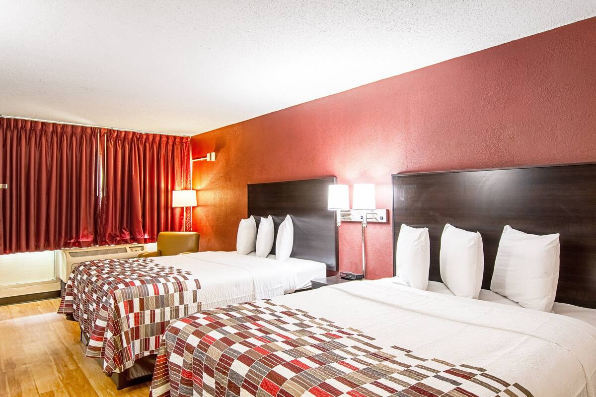A hotel room with two beds, a desk, and a lamp.