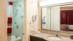 A bathroom with a shower, a sink, a mirror, and a towel rack. - Red Roof Inn Battle Creek (Battle Creek)