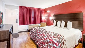 A hotel room with a large bed, red curtains, a desk, and a lamp. - Red Roof Inn Battle Creek (Battle Creek)