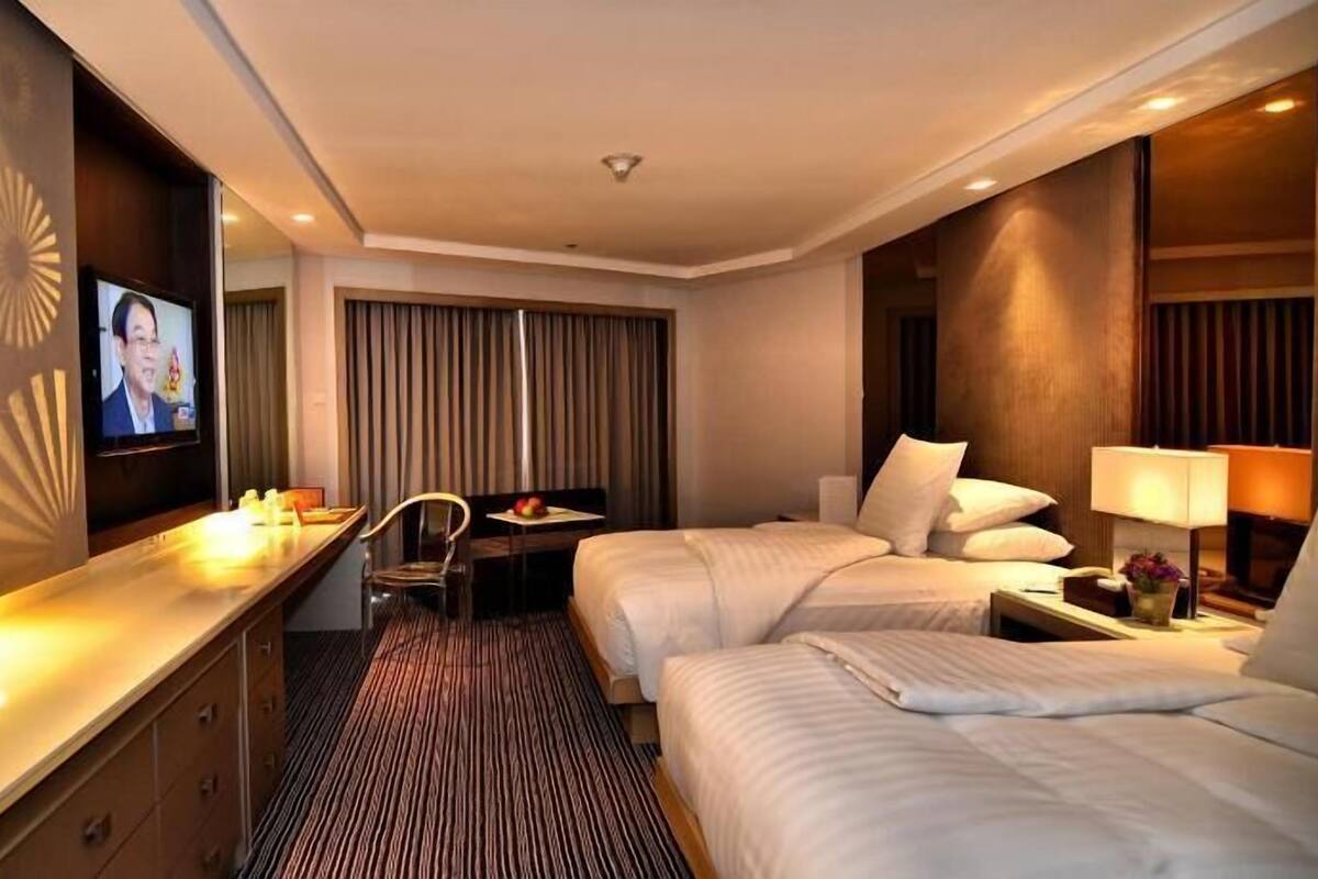 Une chambre d’hôtel comprenant un lit, des tables de chevet, un bureau avec une chaise, une télévision et une grande fenêtre avec des rideaux.
