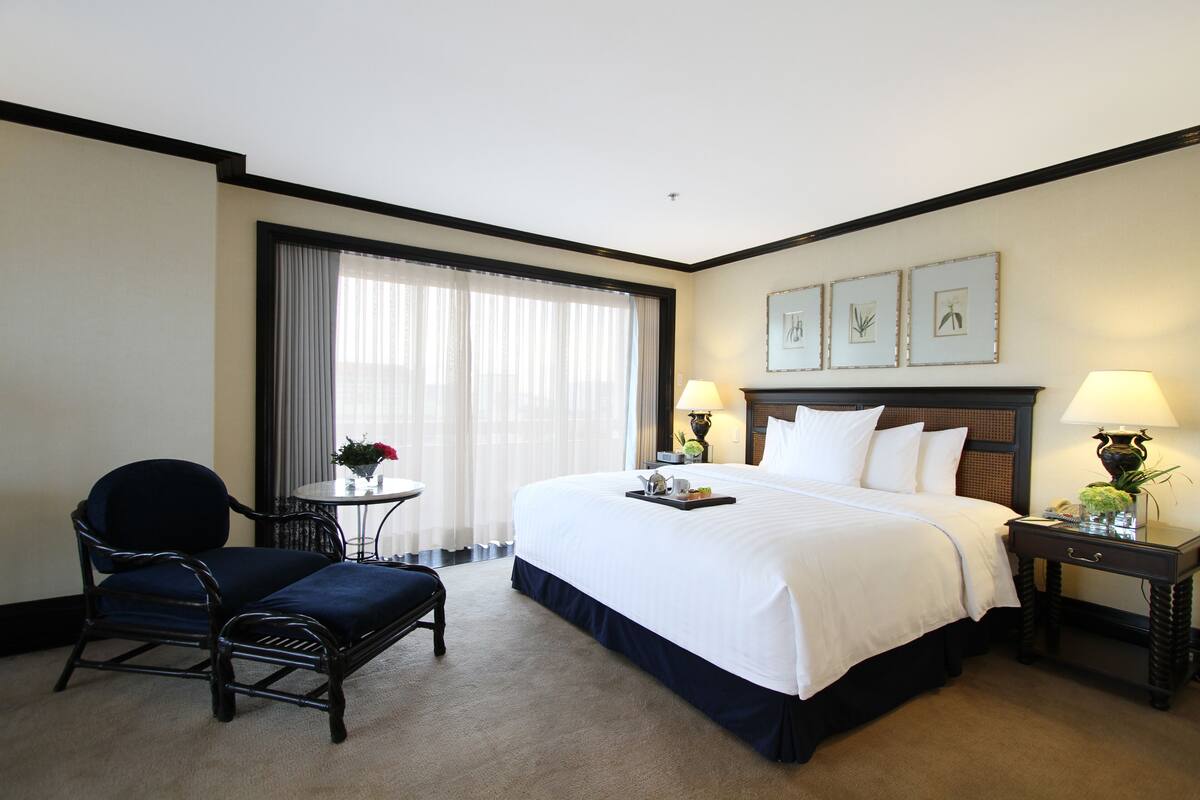 Une chambre d’hôtel avec un grand lit, une chaise, une petite table et une table de chevet avec des lampes.