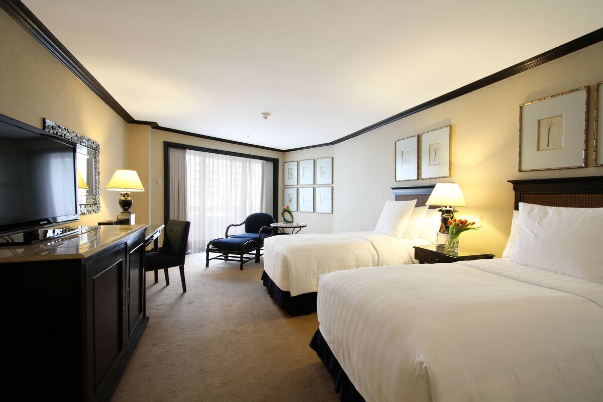 Une chambre d’hôtel avec deux lits, un bureau avec une télévision, une chaise et une fenêtre avec des rideaux.