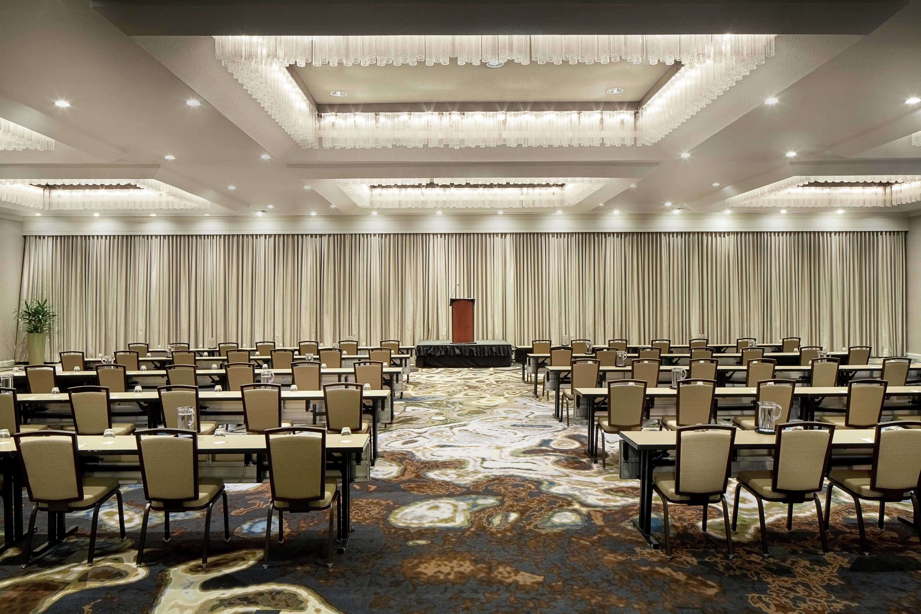 A conference room with rows of tables and chairs, a patterned carpet, and a draped curtain backdrop.