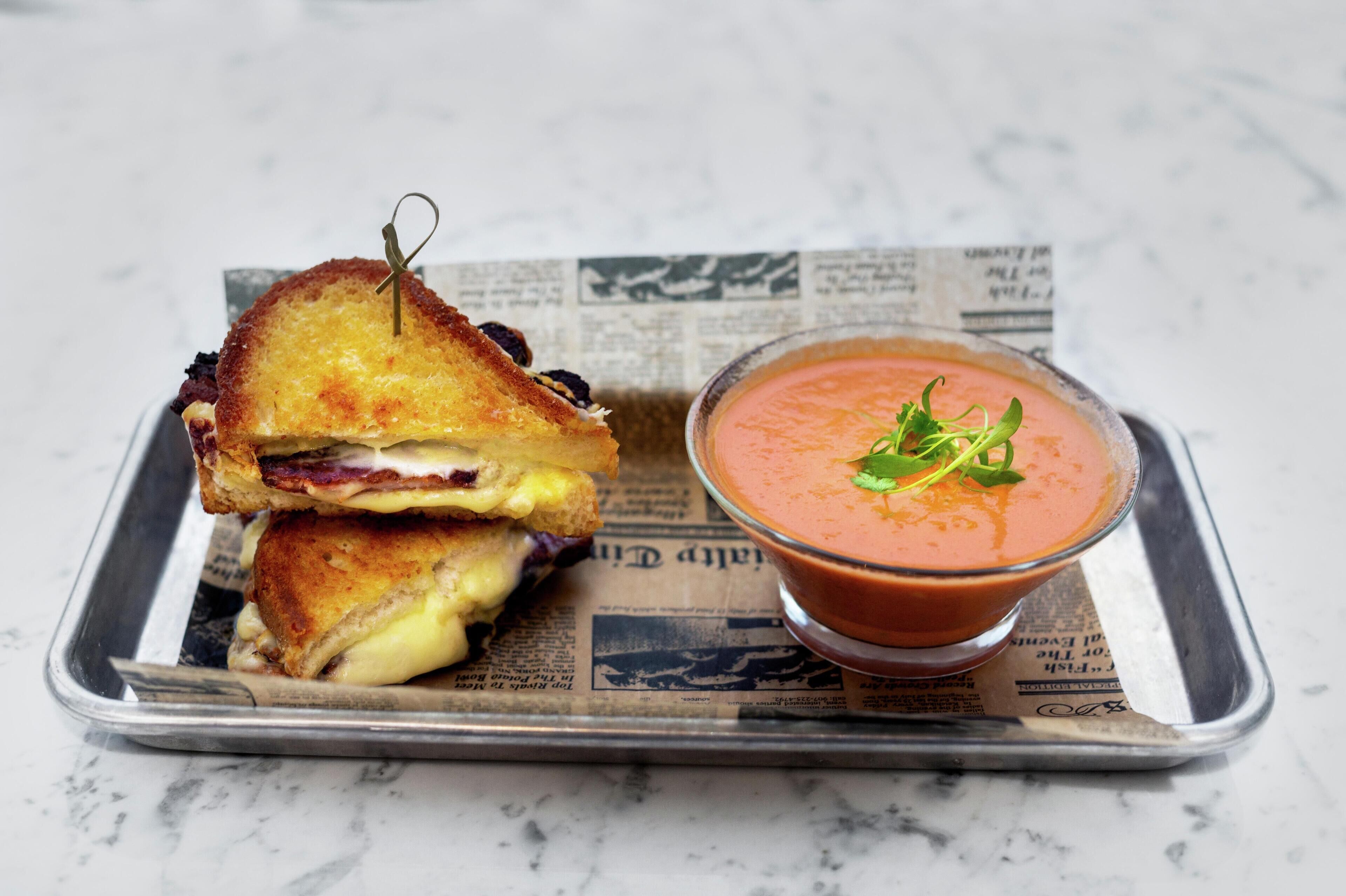 A grilled sandwich and a bowl of soup on a tray.