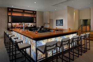 A bar area with a marble countertop, bar stools, and a television mounted on the wall.