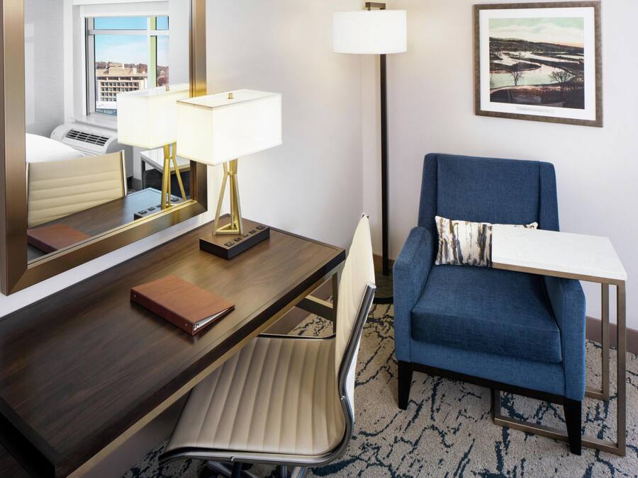 Une chambre d’hôtel équipée d’un bureau, d’une chaise, d’une lampe et d’un tableau encadré au mur.