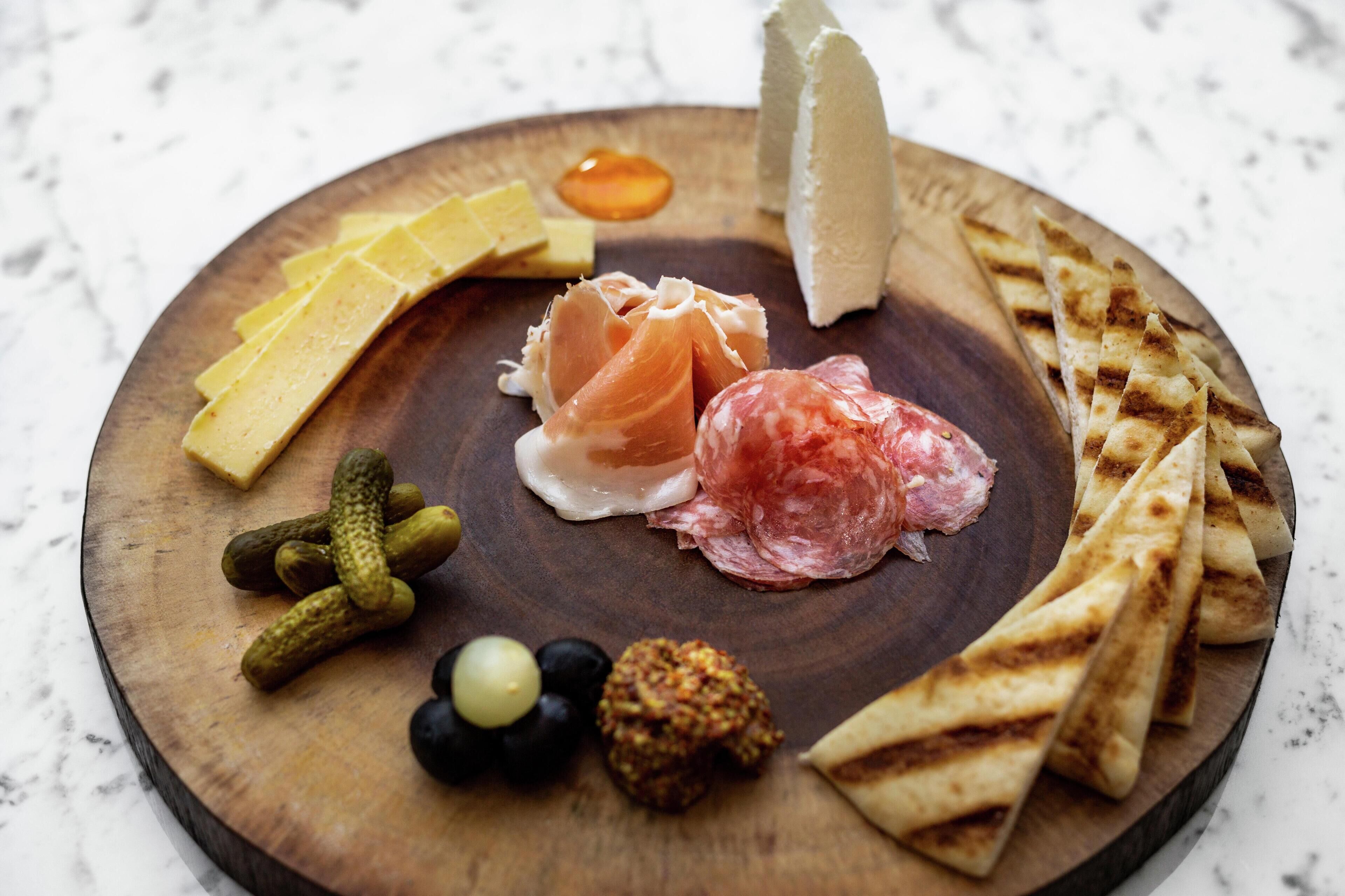 Une planche en bois sur laquelle sont disposés divers aliments, notamment du fromage, de la charcuterie, des cornichons et des galettes.