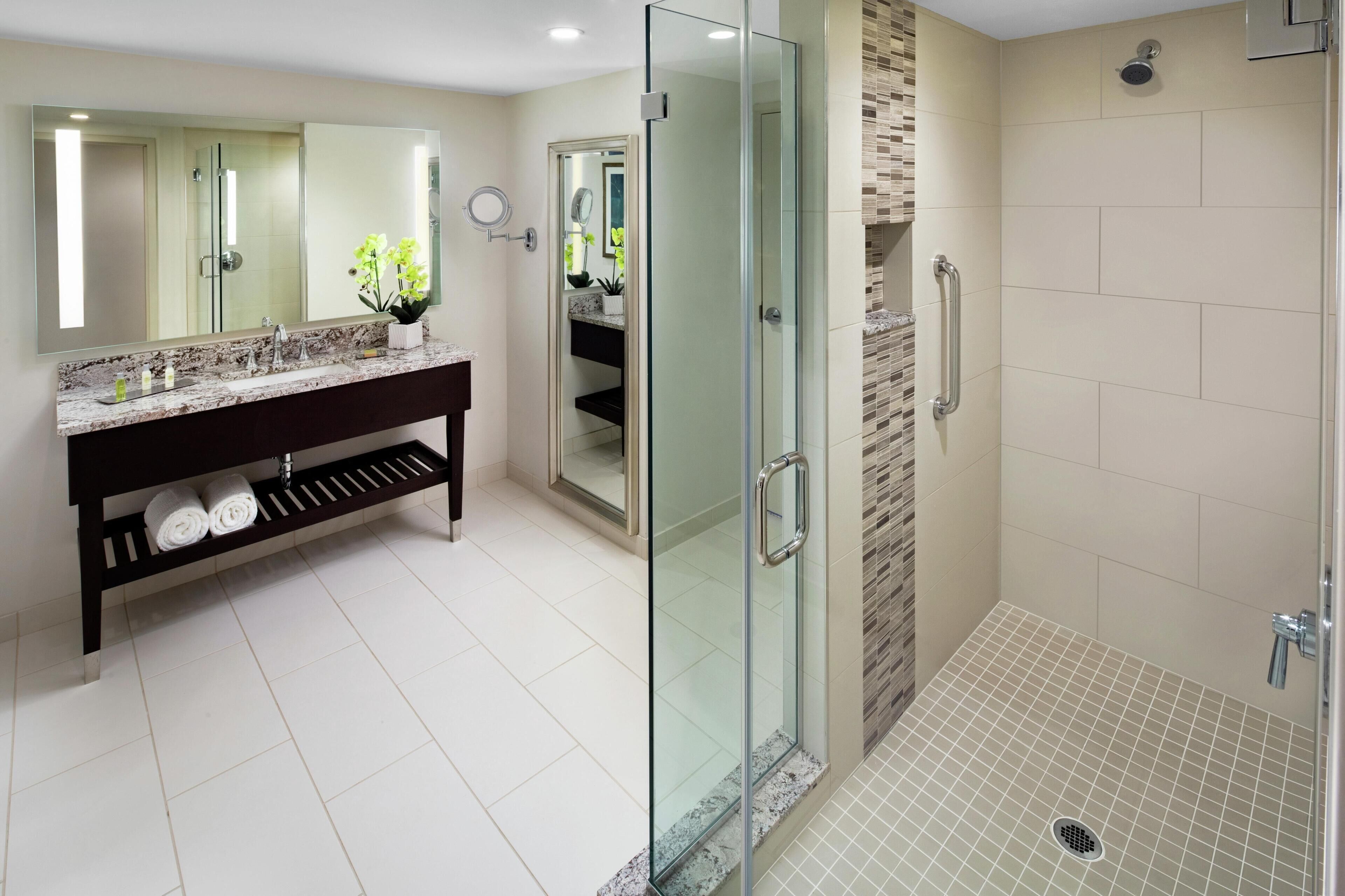 A modern bathroom with a glass-enclosed shower, a vanity with a marble countertop, and a large mirror.