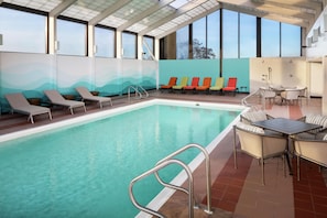 An indoor swimming pool with lounge chairs and a table.
