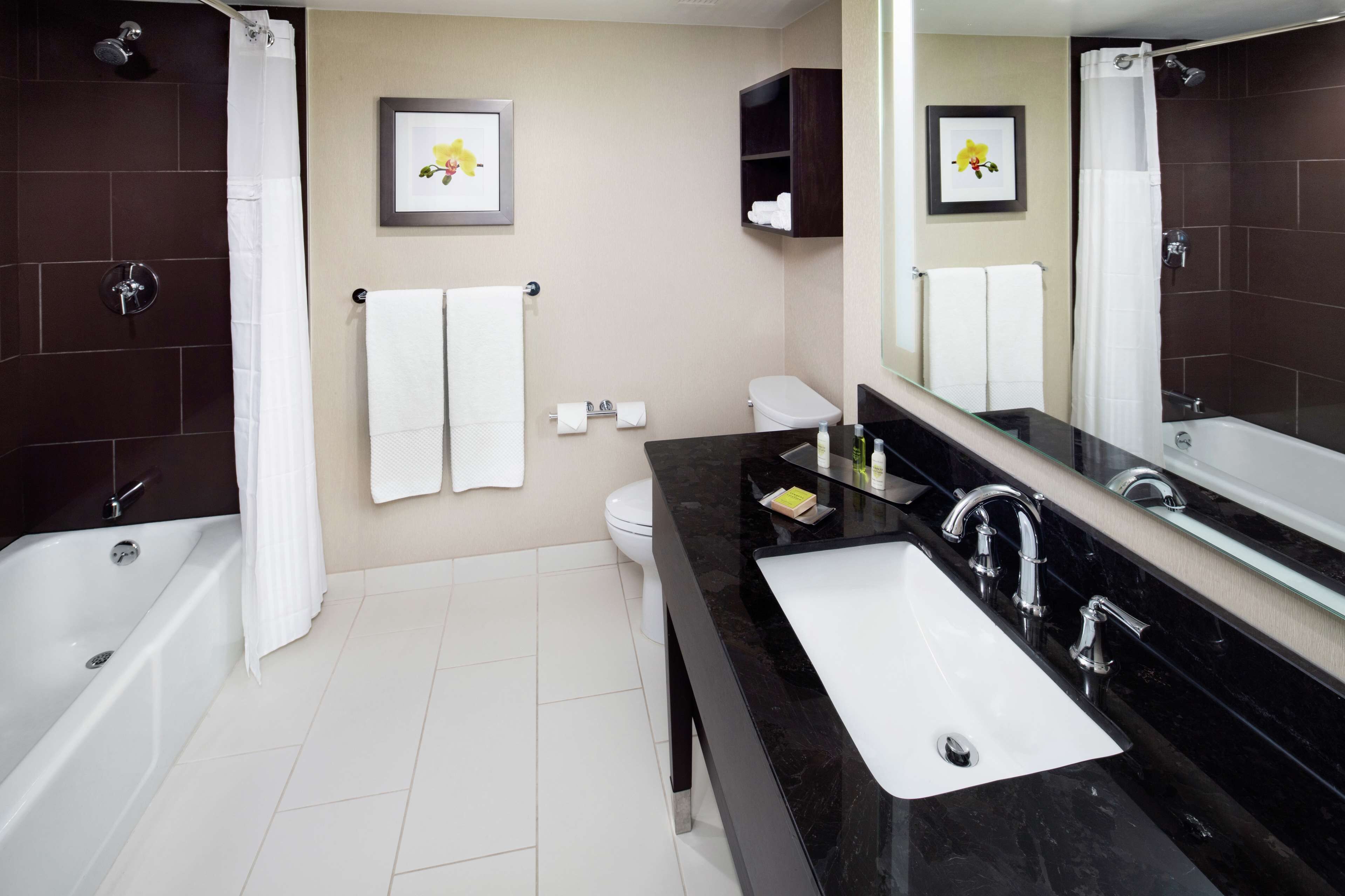 A modern bathroom with a bathtub, a sink, and a toilet. There are two framed pictures on the wall, a shower curtain, and a mirror above the sink.