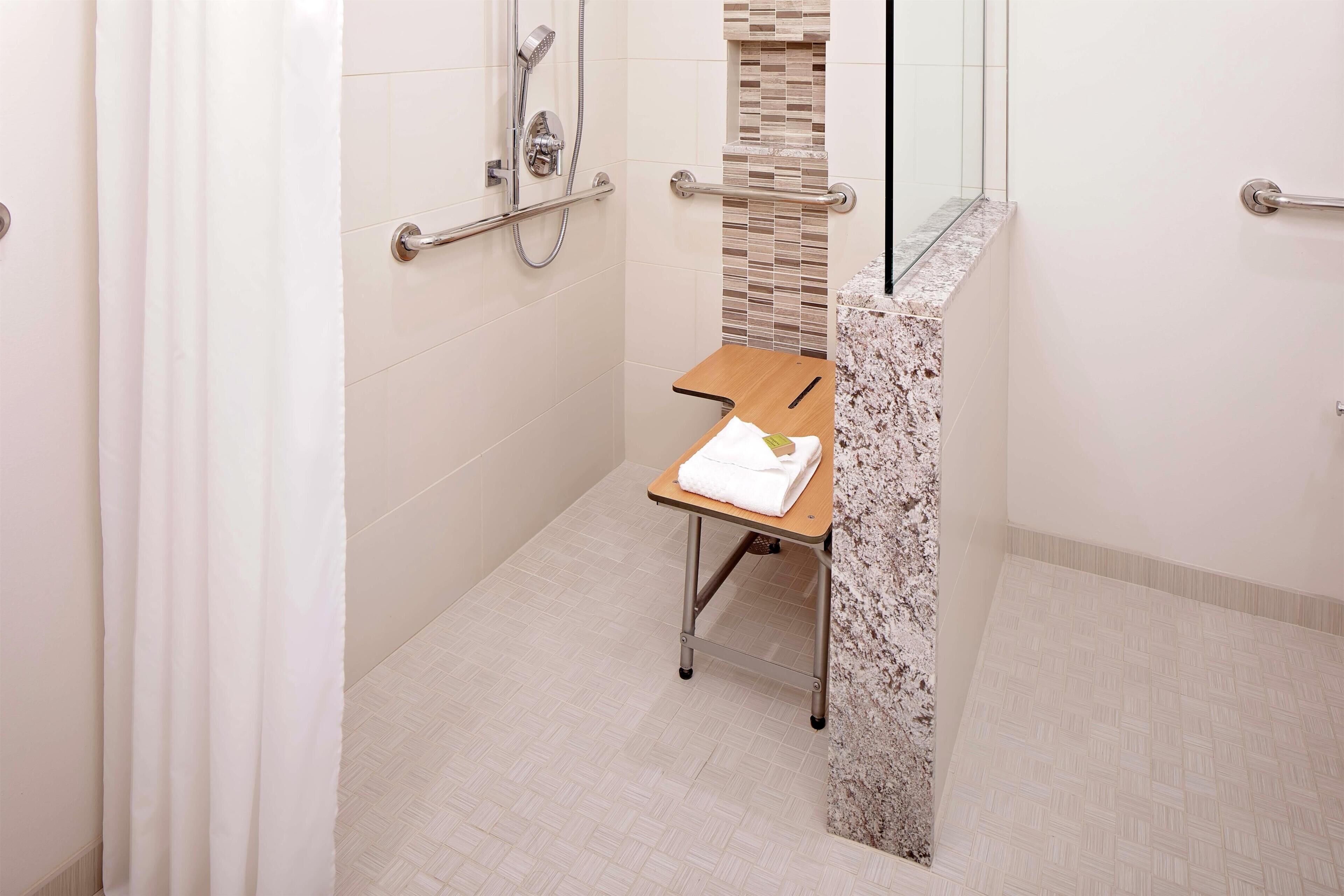 A modern bathroom with a shower, grab bars, a towel rack, and a marble accent wall.