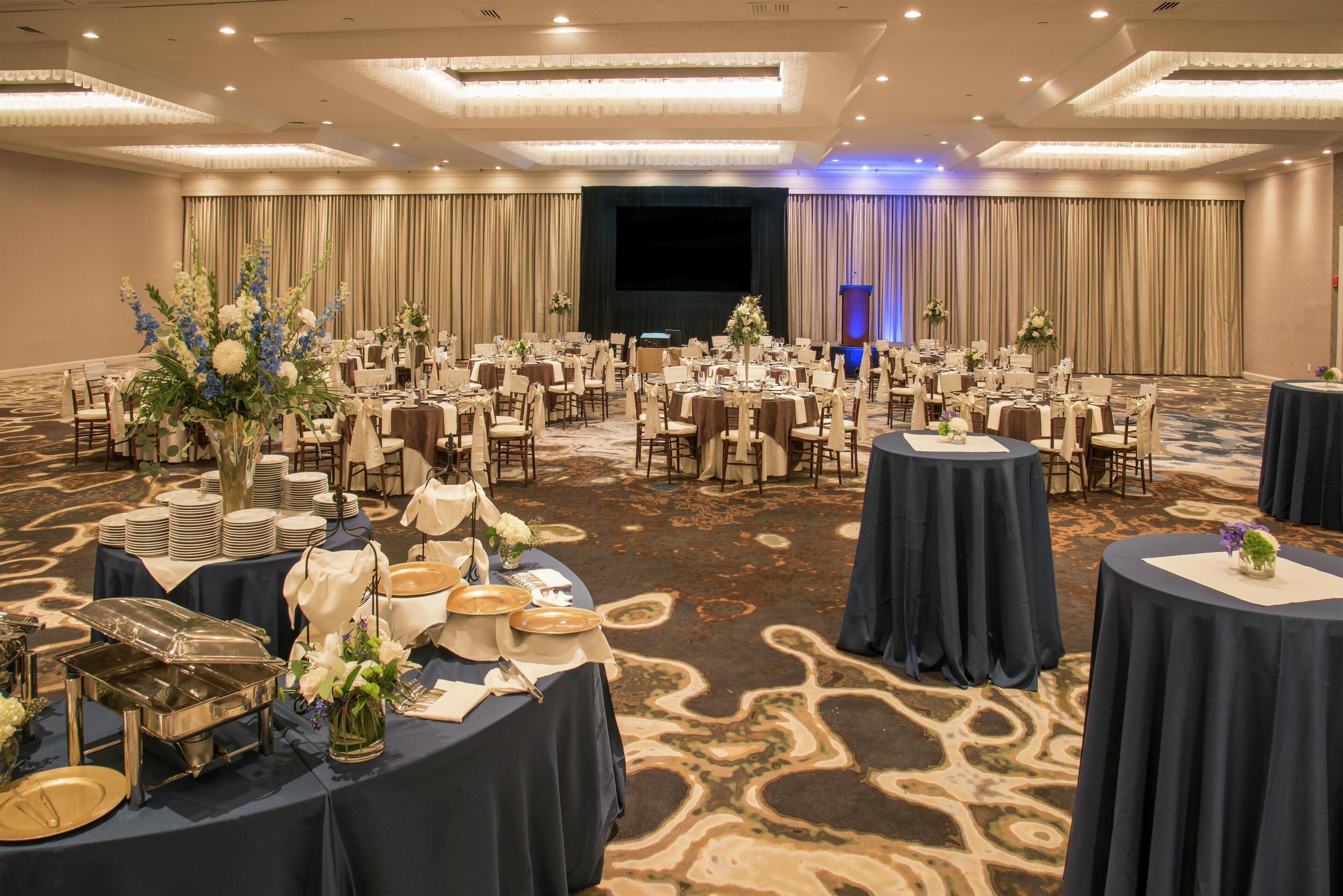 A banquet hall with round tables, chairs, and a stage.
