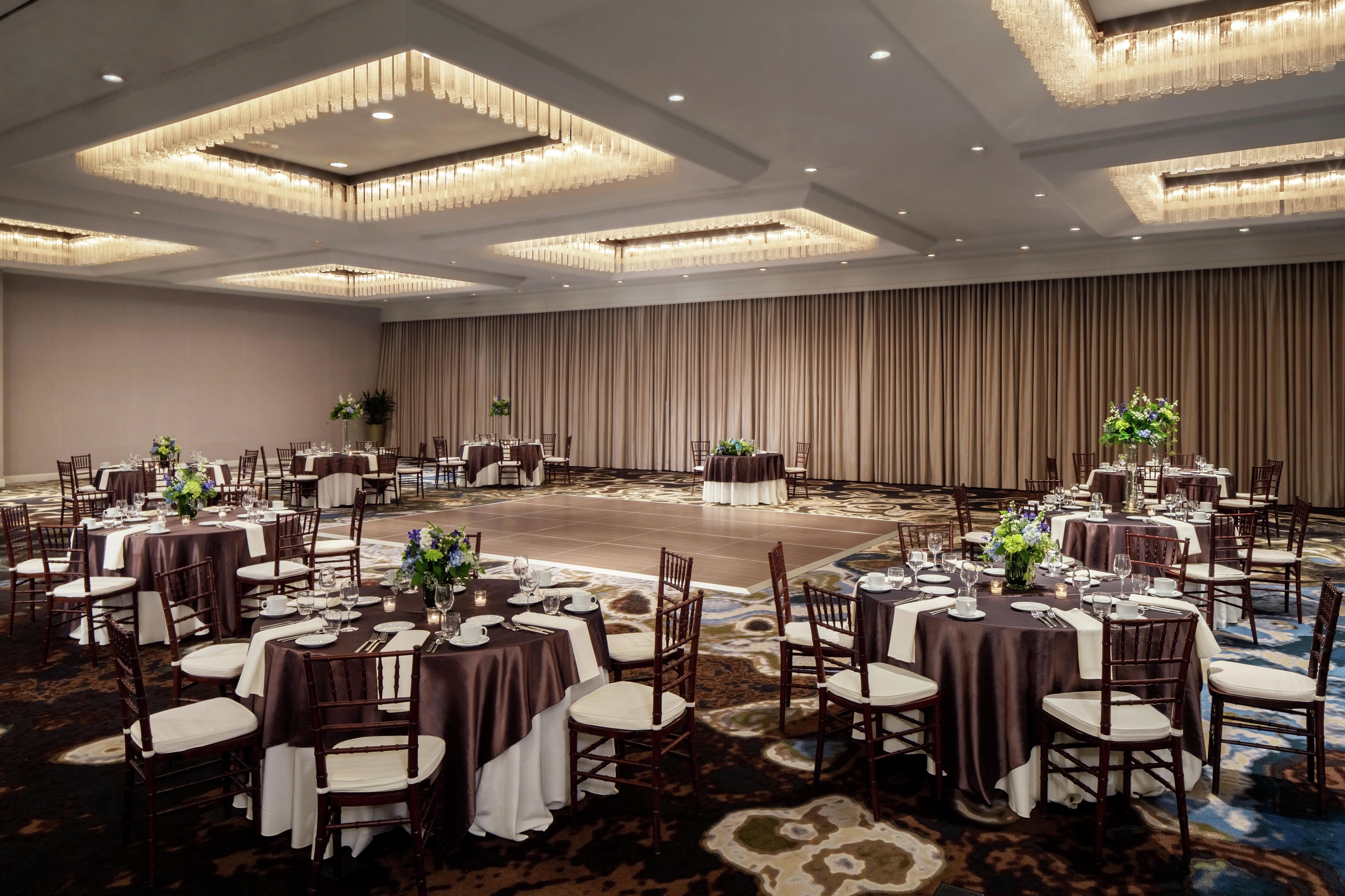 A banquet hall with round tables, chairs, and a large stage.