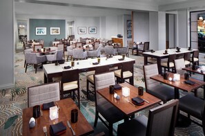 A hotel dining area with multiple tables and chairs, a carpeted floor, and framed artwork on the walls. - DoubleTree by Hilton Manchester Downtown (Manchester)