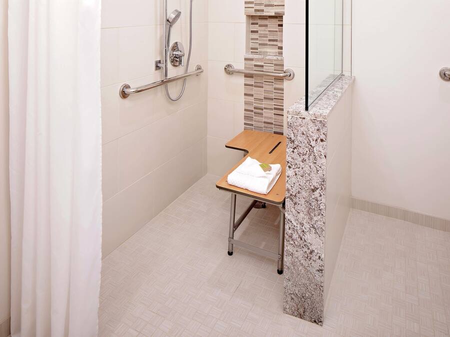 A modern bathroom with a shower, grab bars, a towel rack, and a marble accent wall.