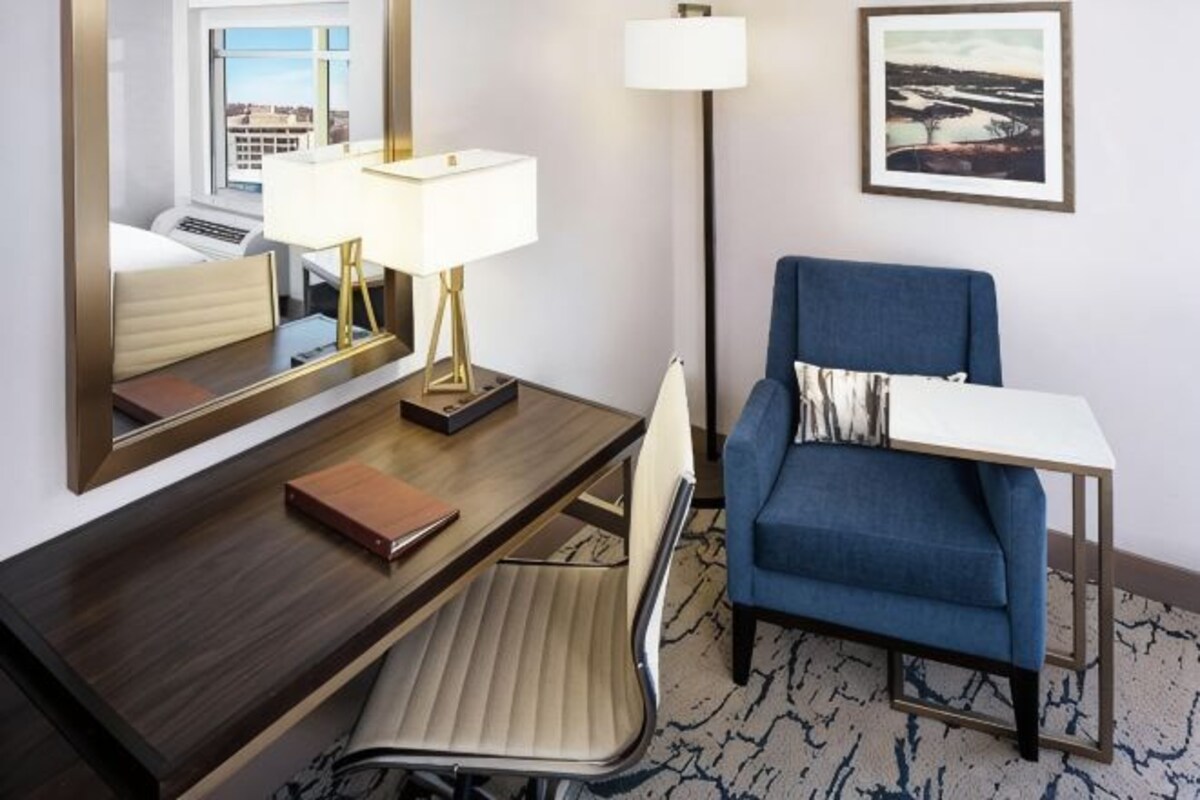 A hotel room with a desk, chair, lamp, and a blue sofa.