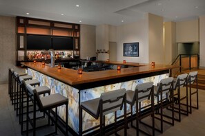 A bar area with a marble countertop, bar stools, and a television mounted on the wall.