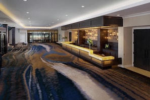 A modern hotel lobby with a long reception desk, seating area, and large windows.