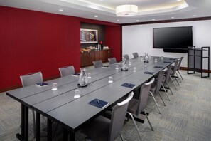 A conference room with a long table, chairs, a flat-screen TV, and a red accent wall. - DoubleTree by Hilton Manchester Downtown (Manchester)