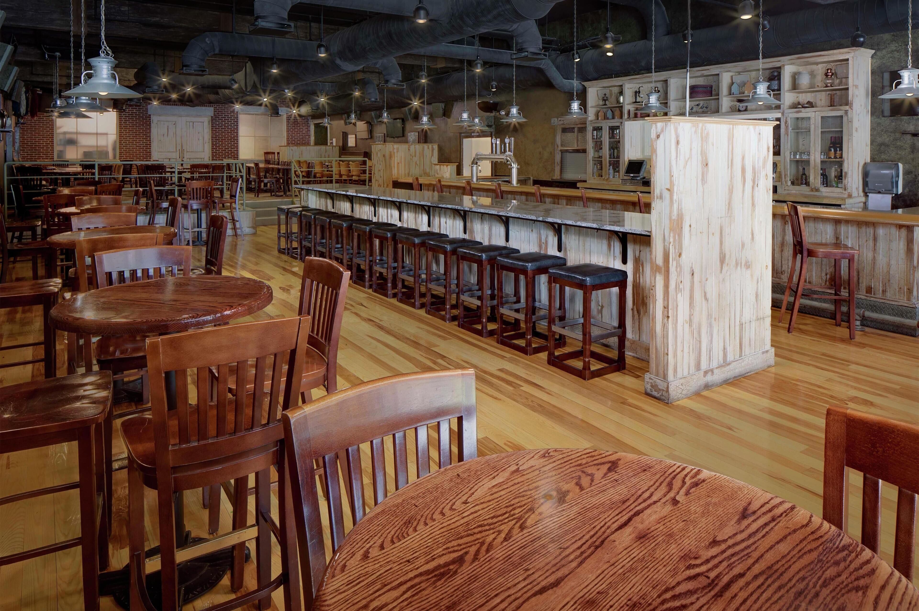 A restaurant with wooden tables and chairs, a bar area, and brick walls.