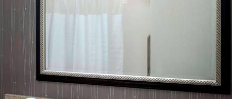 Un baño con un espejo grande, un lavabo y artículos de aseo en la encimera.