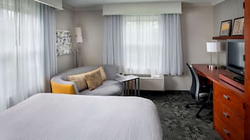 Hotelkamer met een groot bed, een bureau, een stoel, een televisie en een raam met gordijnen.