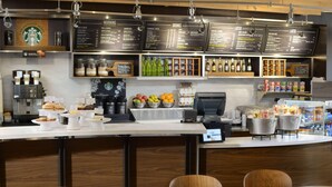 Interior de uma cafeteria Starbucks, com quadro de menu, máquinas de café, caixa registradora e área de estar.