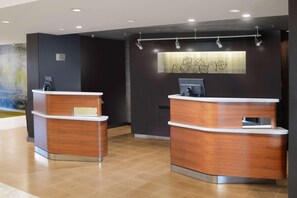 A reception area with two wooden reception desks, a digital screen, and a wall-mounted artwork. - Courtyard by Marriott Dallas North (Dallas)
