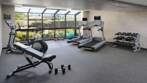 Academia com esteiras, elíptico, banco, halteres e kettlebell.