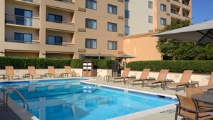 Piscina com espreguiçadeiras e guarda-sóis, rodeada por um edifício com varandas.