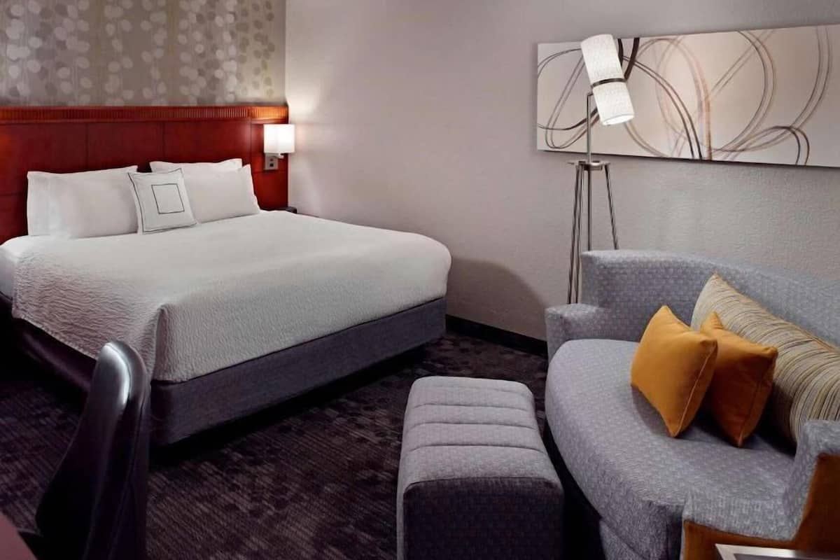 A hotel room with a large bed, a sofa, a desk, and a wall-mounted lamp.