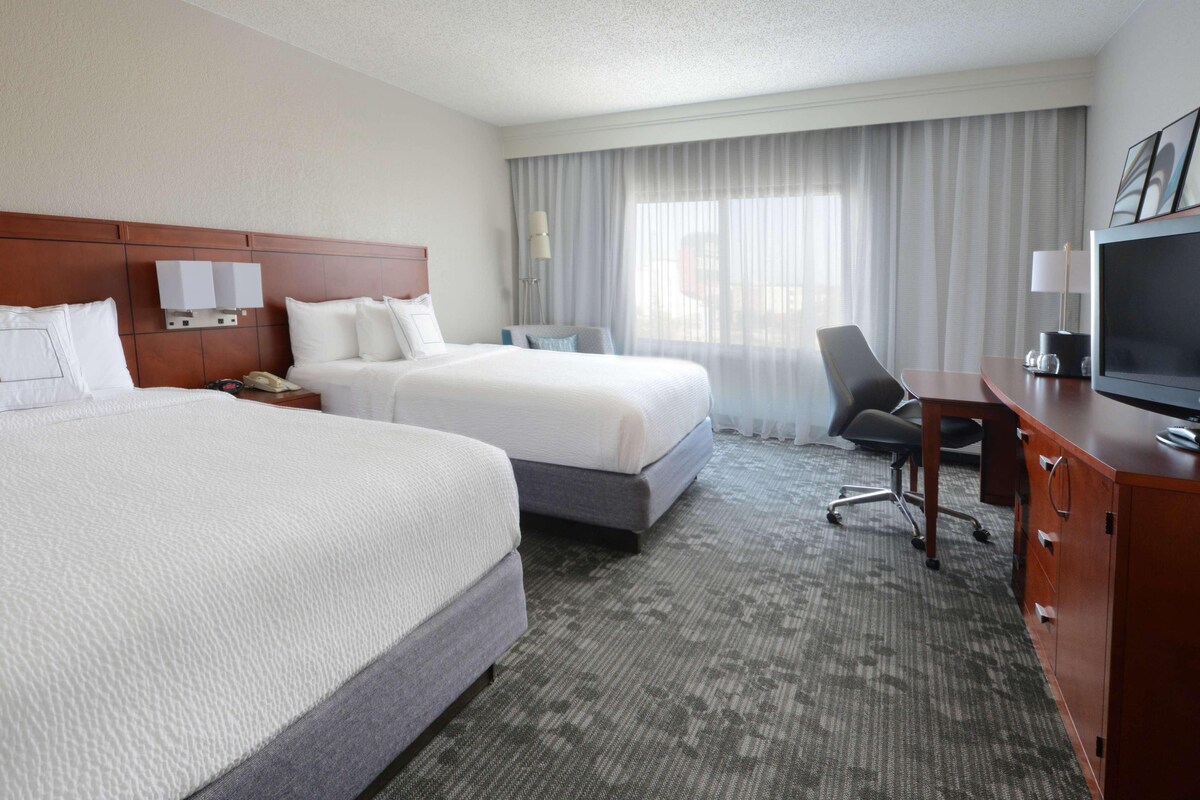 A hotel room with two beds, a desk with a television, and a chair.