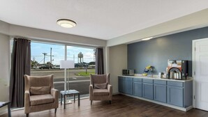 A modern hotel room with a large window, two armchairs, a small table, a kitchenette with a microwave, coffee maker, and a TV. - Econo Lodge Cherry Point (Havelock)