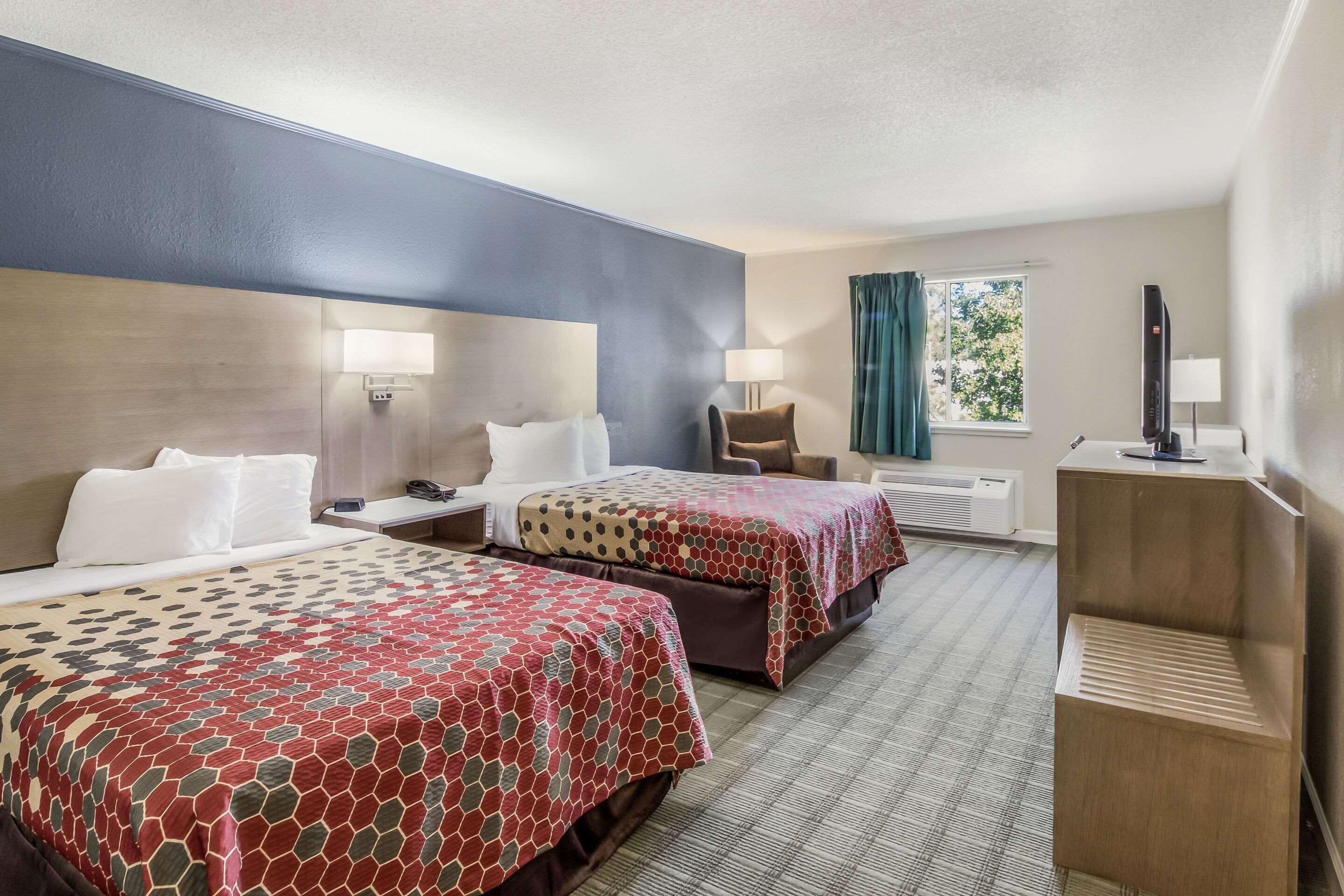A hotel room with two beds, a desk, a chair, a TV, and a window with curtains.