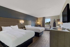 Habitación de hotel con dos camas, un escritorio, un televisor y ventana con vista al exterior.
