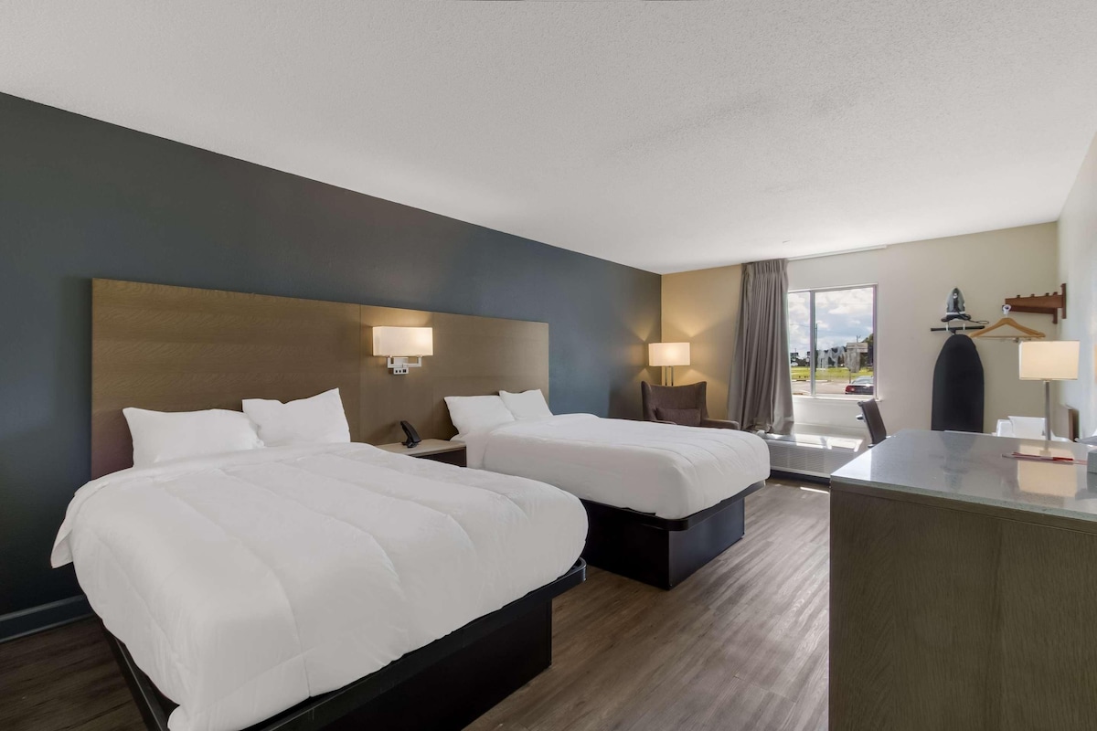 A hotel room with two beds, a desk, and a view of the outdoors.