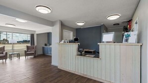 A reception area with a wooden counter, seating, and a view through large windows. - Econo Lodge Cherry Point (Havelock)