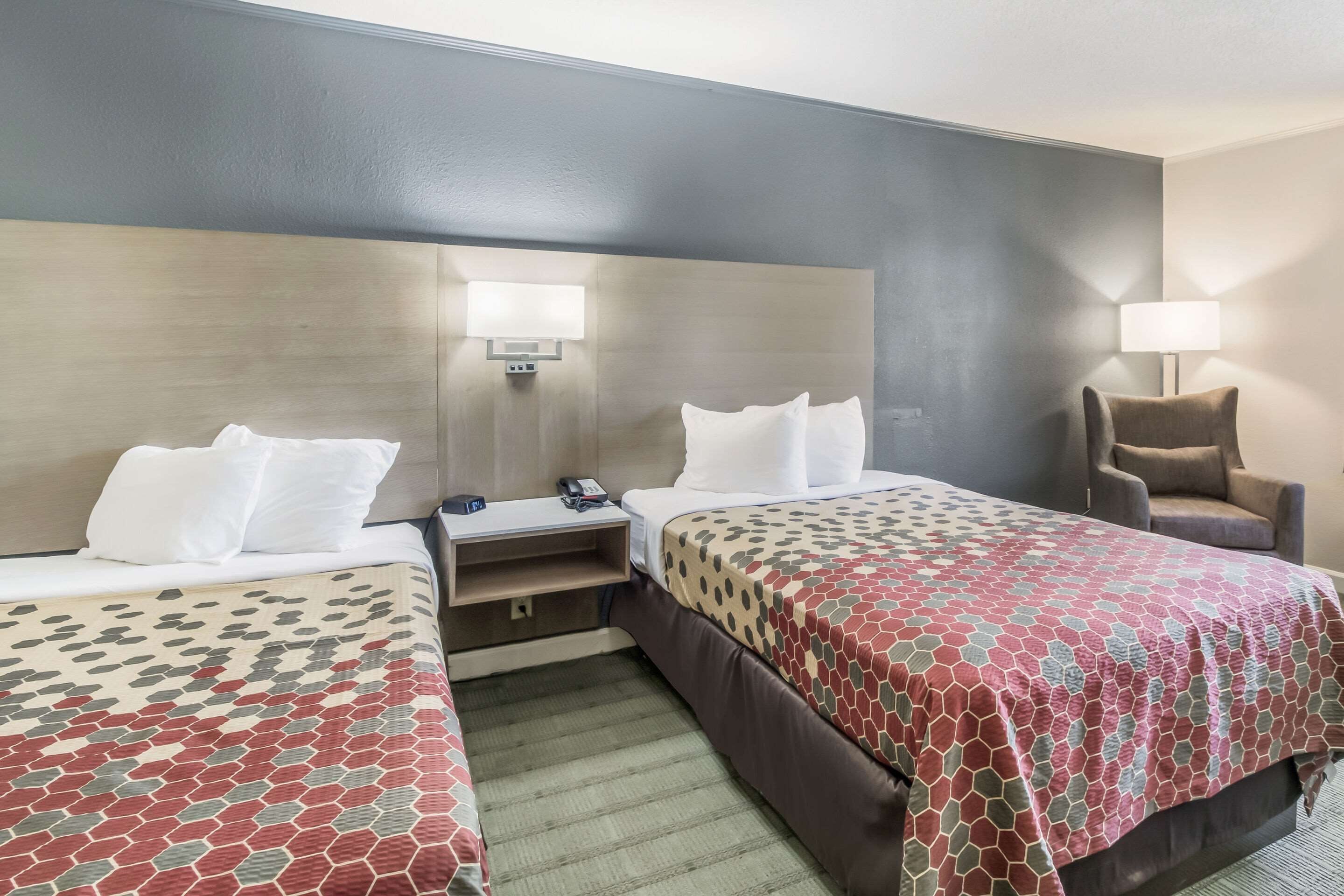 Una habitación de hotel con dos camas, una mesita de noche, una silla y una lámpara.