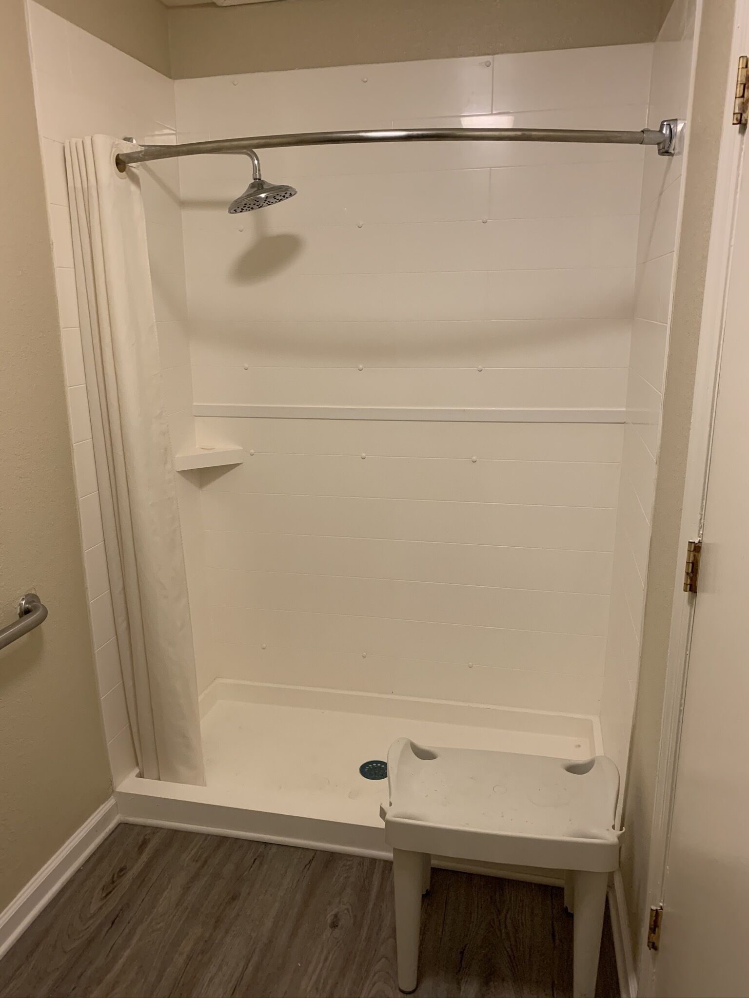 Une douche à l’italienne avec un pommeau de douche, une petite étagère et une porte dotée d’une poignée.