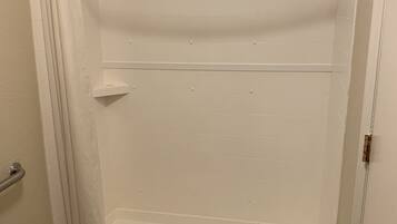 Une douche à l’italienne avec un pommeau de douche, une petite étagère et une porte dotée d’une poignée.