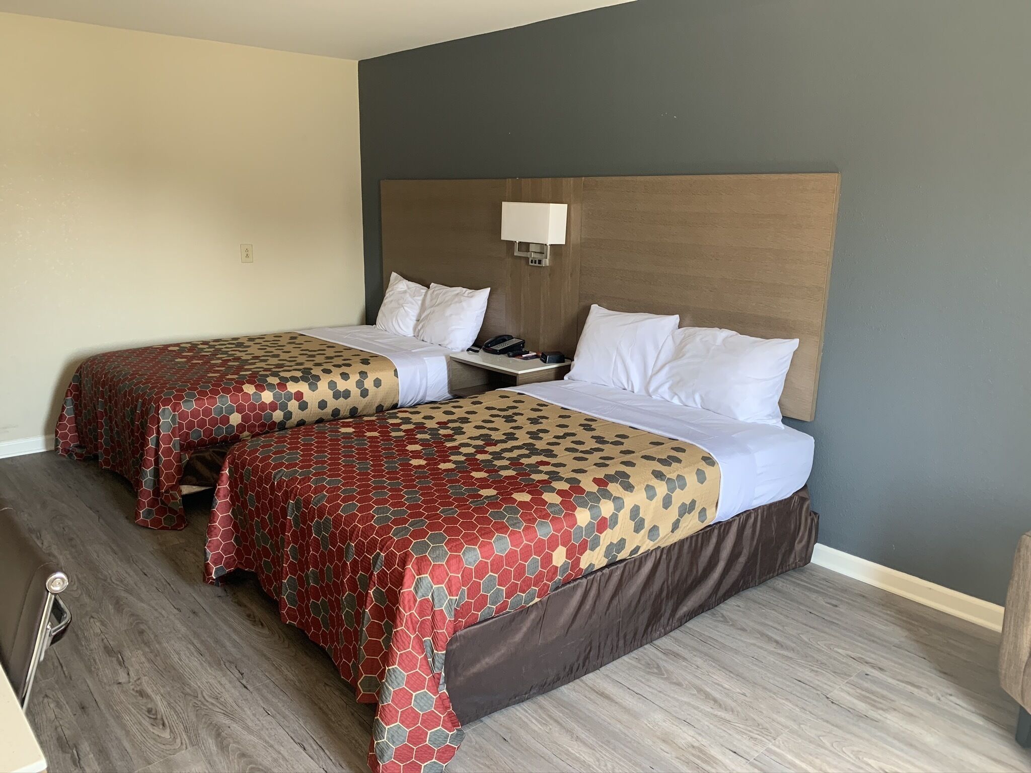 Ein Hotelzimmer mit zwei Betten, jeweils mit einem gemusterten Überwurf und weißen Kissen. An einer Seite befindet sich ein Nachttisch mit Lampe und Telefon.