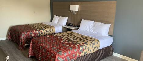 Ein Hotelzimmer mit zwei Betten, jeweils mit einem gemusterten Überwurf und weißen Kissen. An einer Seite befindet sich ein Nachttisch mit Lampe und Telefon.