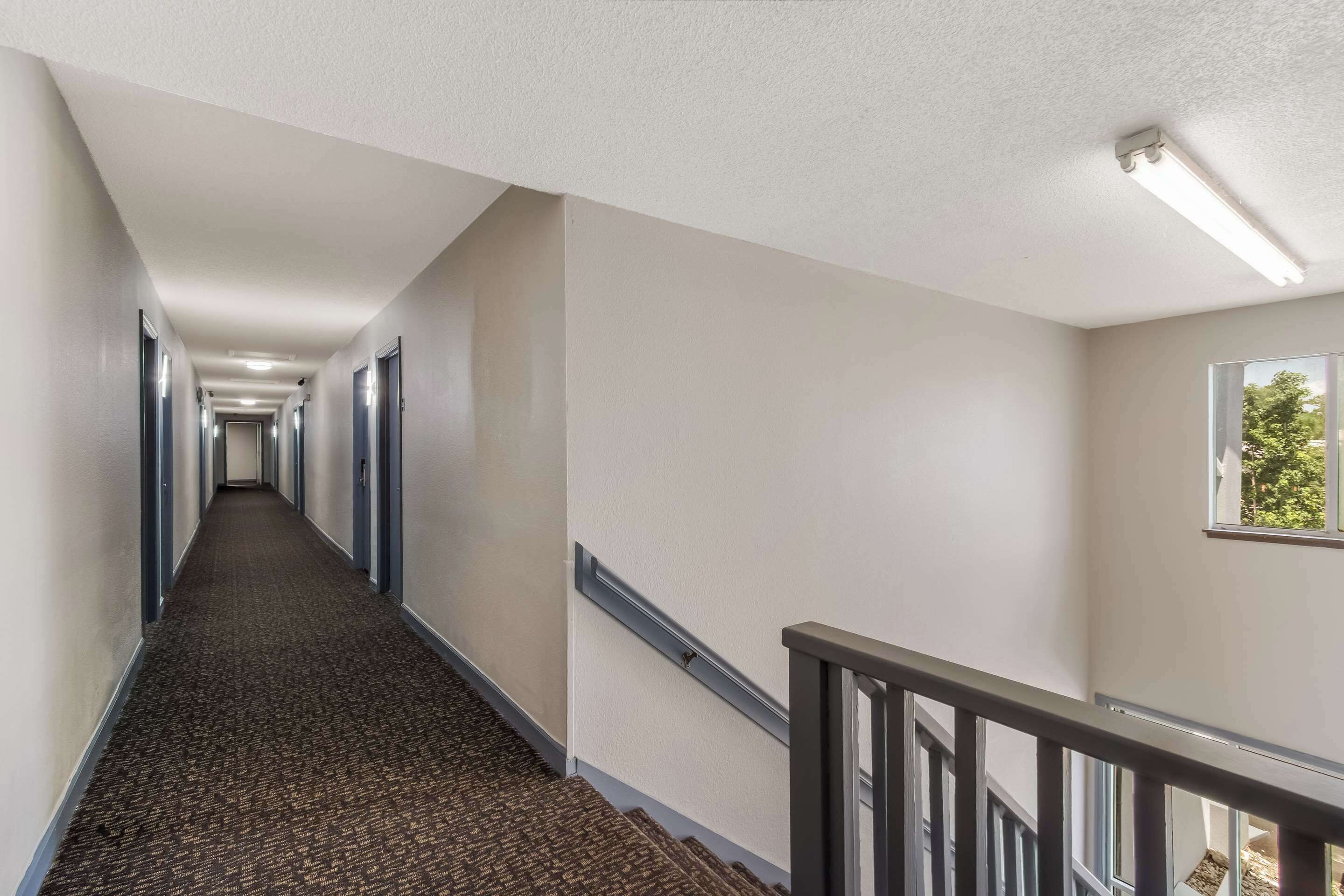 A long, narrow hallway with carpeted floors, a handrail on the right, and a window on the far wall.