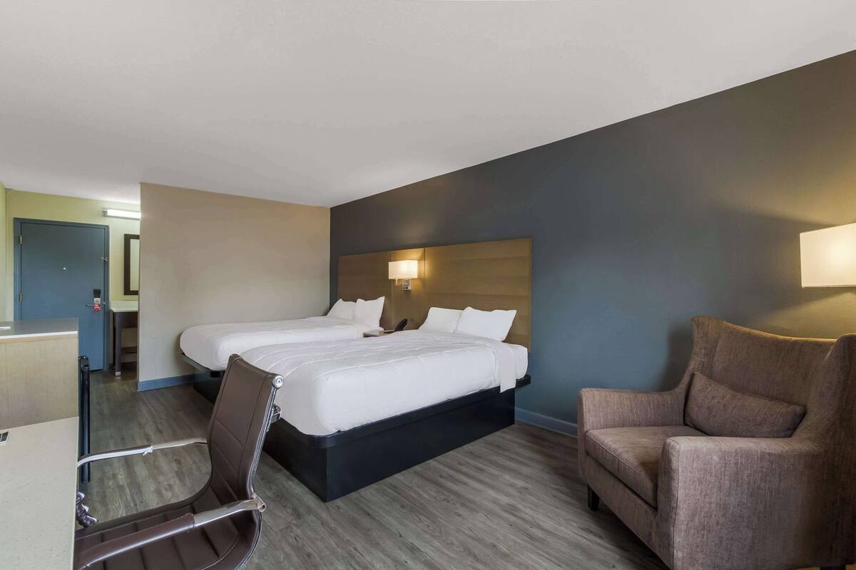 A hotel room with two beds, a desk, a chair, and a couch.