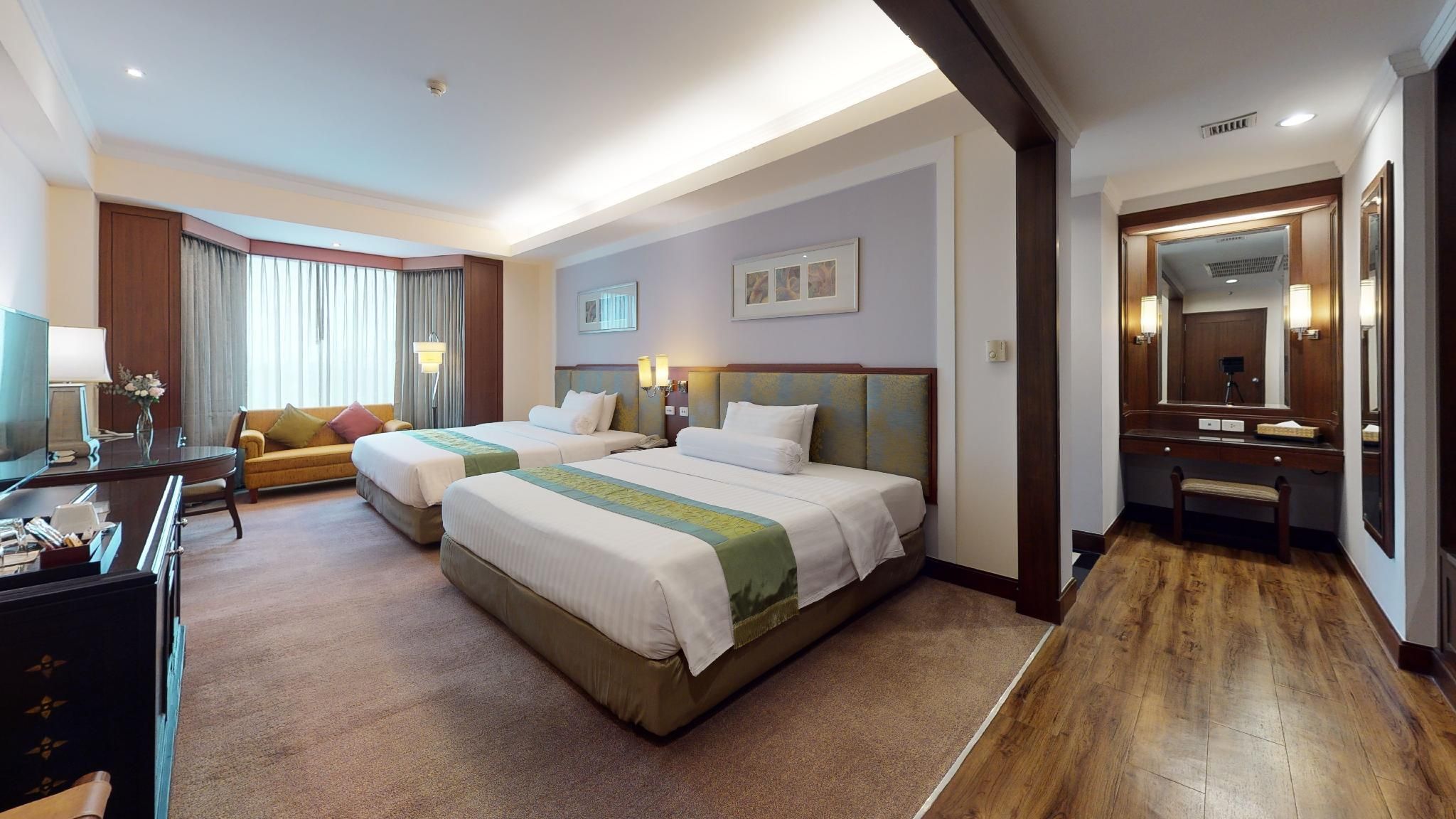 A hotel room with two beds, a desk, a chair, a TV, and a bathroom.