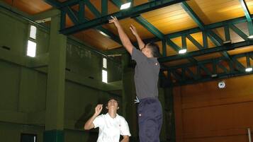 A basketball court with a hoop, a player jumping towards it, and another player watching.