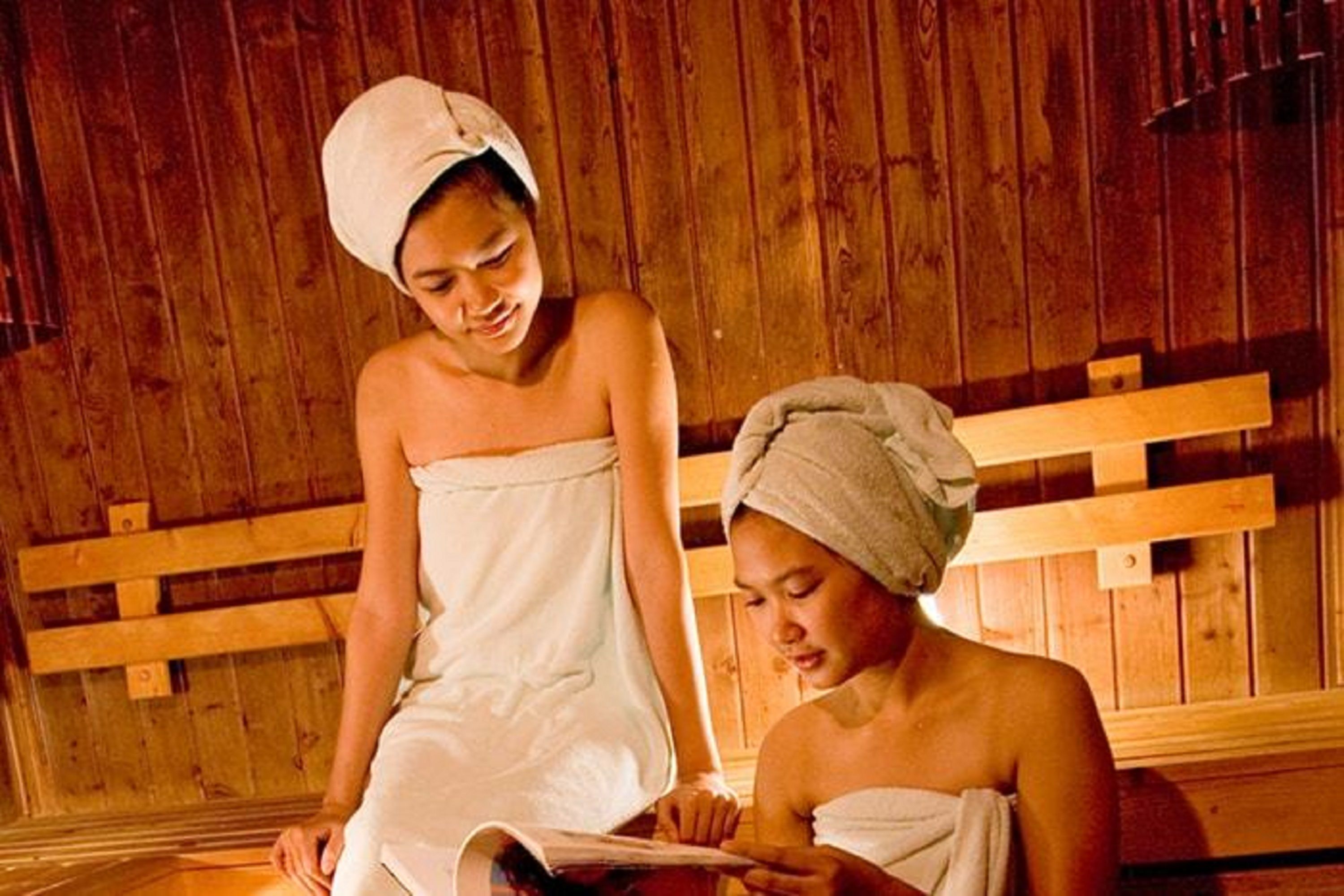 Two people in a wooden room with benches, one reading a book.