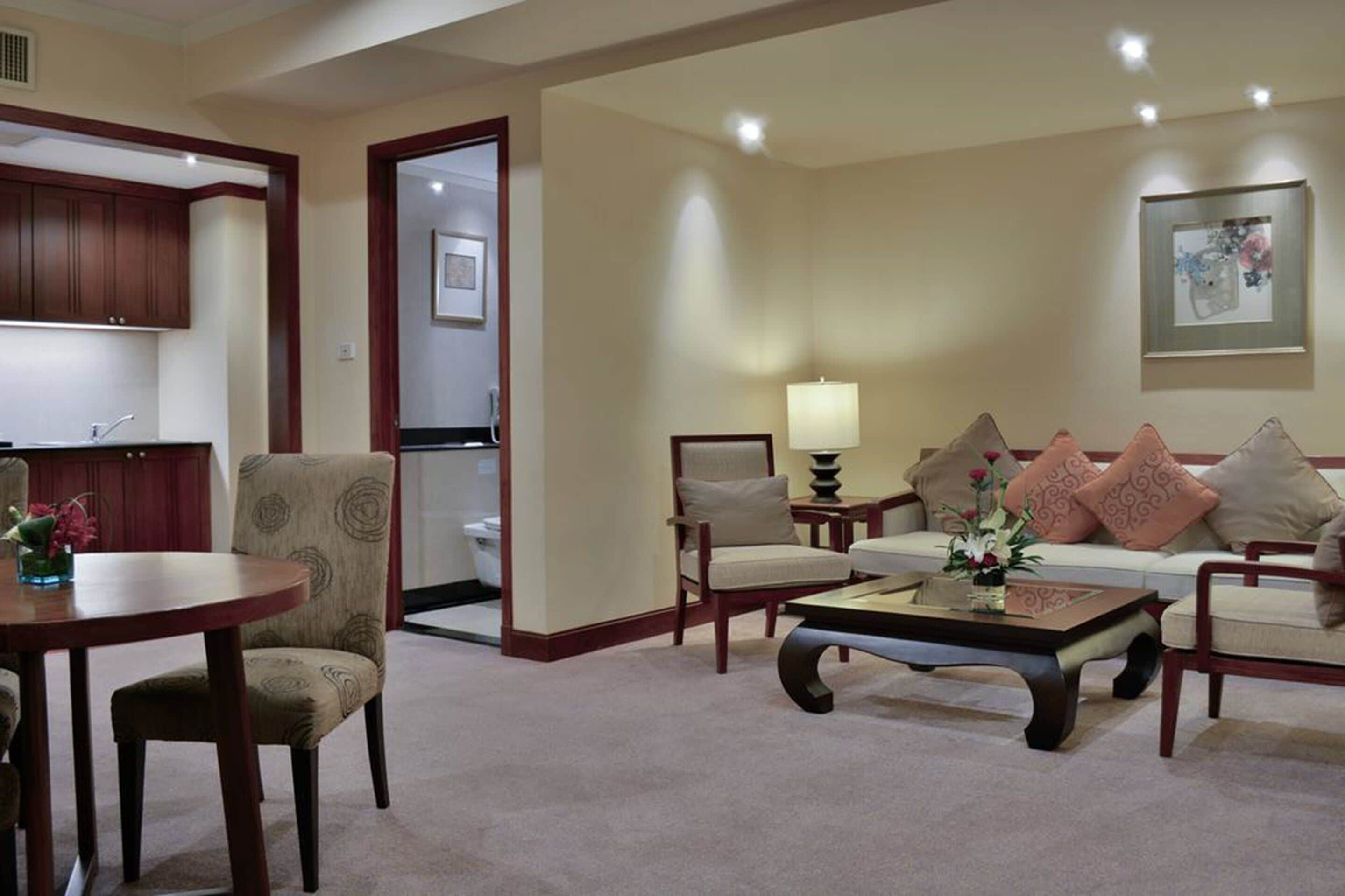 A hotel room with a dining area, a sofa set, and a kitchen visible through an open door.