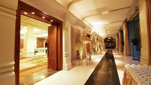 A hotel corridor with a long reception desk, a carpeted area with tables and chairs, and a statue of an elephant. - Rama Gardens Hotel Bangkok (Bangkok)