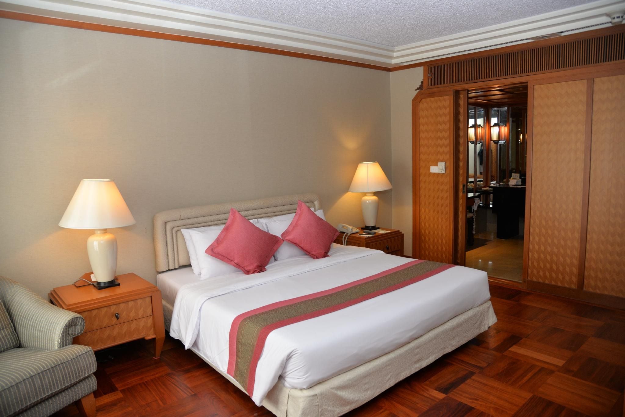 A hotel room with a large bed, two bedside lamps, a wooden wardrobe, and a wooden floor.